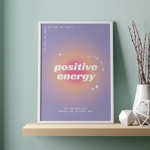 May include: A white framed print with a purple background and a pink and orange gradient circle with stars. The text on the print reads "YES GIRL YOU CAN positive energy THE UNIVERSE WILL SUPPORT YOU IN EVERY WAY."