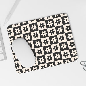 May include: A black and white checkered mouse pad with a white mouse on top. The mouse pad has a repeating pattern of small black flowers on a white background and white flowers on a black background.