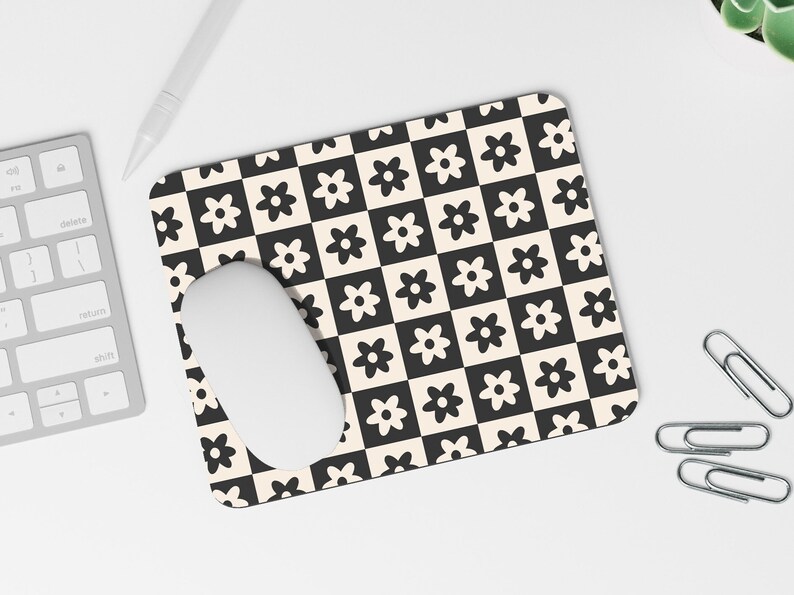 May include: A black and white checkered mouse pad with a white mouse on top. The mouse pad has a repeating pattern of small black flowers on a white background and white flowers on a black background.