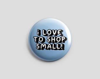 Könnte beinhalten: Ein runder Ansteckbutton mit hellblauem Hintergrund. Der Text I LOVE TO SHOP SMALL! ist in Weiß mit einem dicken schwarzen Schlagschatten aufgedruckt und zeigt eine kräftige, abgerundete und verspielte Schriftart, die mittig platziert ist.