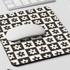 May include: A black and white checkered mouse pad with a daisy pattern. A white computer mouse is on top of the mouse pad.