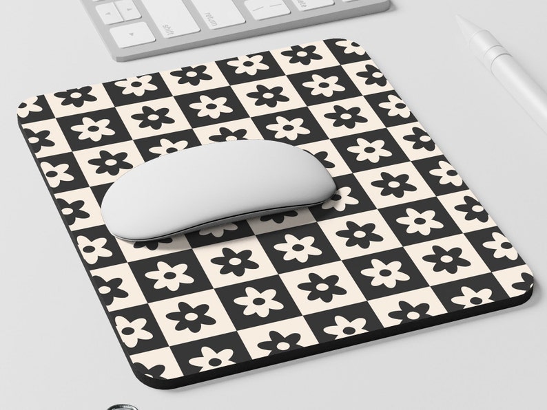 May include: A black and white checkered mouse pad with a daisy pattern. A white computer mouse is on top of the mouse pad.