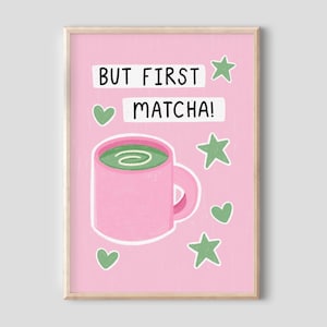 May include: A framed print with a pink background featuring the text "BUT FIRST MATCHA!" in white. A pink mug with green matcha and green star and heart shapes surround the text. The print has a light wood frame.