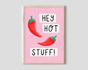 May include: A framed art print featuring two red chili peppers with green stems against a pink background. The words "HEY HOT STUFF!" are written in black on white rectangular blocks. The artwork has a playful, illustrative style.