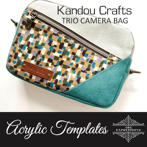May include: A rectangular camera bag with a patterned front in teal, brown, purple, and white. The bag has a gray top and teal side panel. The text "Kandou Crafts TRIO CAMERA BAG" is visible. A leather tag reads "KANDOU".