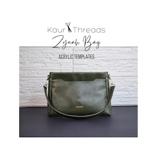 May include: A dark green leather shoulder bag with a zipper closure and a front pocket. The bag has a gold-colored zipper pull and a gold-colored nameplate on the front. The bag is on a black surface. Kaur Threads Zynah Bag ACRYLIC TEMPLATES