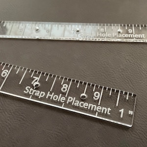 May include: Two clear plastic rulers with markings for strap hole placement. The top ruler is labeled "Hole Placement 3/4" and the bottom ruler is labeled "Strap Hole Placement 1".