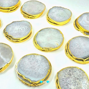 Könnte beinhalten: Eine Sammlung von Untersetzern aus Achat mit goldfarbenem Rand. Die Untersetzer haben ein natürliches, hellgraues und weißes Farbmuster. Die goldenen Ränder verleihen dem Naturstein einen Hauch von Eleganz.