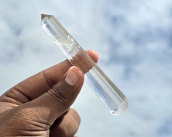 以下が含まれることがあります： 一端が六角形のファセットカットされたポイントで、本体が滑らかな円筒形をしている透明なクォーツクリスタルのワンド。無色透明なクリスタルには自然な内部インクルージョンが見られ、表面で光を反射しています。