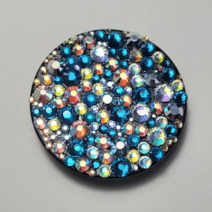 Peut inclure: Une poignée de téléphone ronde noire avec un motif coloré de strass bleus, orange et argent.