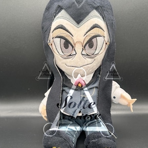 May include: A plush doll featuring a character with pale skin, dark hair, and round gold-rimmed glasses. The doll wears a black hooded cloak, a grey vest over a white shirt, and blue plaid pants. Yellow gear-shaped patches are on the feet.