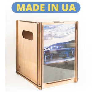 Puede incluir: Una caja de madera con un panel frontal transparente que muestra un tablero de instrumentos de automóvil vintage sobre un fondo azul y blanco. La caja tiene un recorte en el lateral y el texto "MADE IN UA" está impreso sobre un fondo azul.