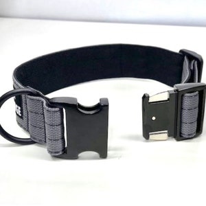 May include: A black and gray dog collar with a metal buckle and a D-ring. The collar is made of a durable, woven material.