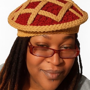 Peut inclure: Un chapeau au crochet fait à la main en forme de tarte, avec une garniture rouge et une croûte en treillis beige. Le chapeau est porté par une personne portant des lunettes. Le texte "CROCHET by nae" est en haut.
