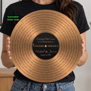 May include: A circular copper-colored plaque designed like a vinyl record, featuring the song lyrics to Thinking Out Loud spiraling around the edge. The center black label displays the text Thinking Out Loud, 19TH ANNIVERSARY, Michael & Jessica, August 6, 2018, and a sound wave graphic. A green Scannable Music Code label is visible.
