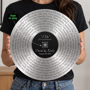 以下が含まれることがあります： レコード盤を模した円形の銀色のプレート。中央の黒いラベルには「I Do」「10th Anniversary」「David & Kathy」「August 20, 2006」の文字、QRコード、緑色の「Scan to play」タグが記されている。銀色の部分には刻印されたテキストがある。