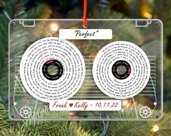 May include: A clear plastic cassette tape ornament with a red string for hanging. The cassette tape has a white label with black text that reads "Perfect" and lyrics from the song "Perfect" by Ed Sheeran. The cassette tape also has a red heart and the text "Frank Kelly - 10.11.22".
