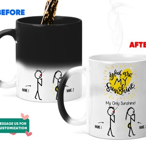 May include: A black and white color-changing mug with a stick figure couple on one side and the text "You are my sunshine. My only sunshine!" on the other side. The mug is empty and has a white interior.