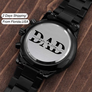 May include: Black wristwatch with a silver face and a personalized inscription that reads "DAD" with the names "Kyle" and "Lily" underneath.