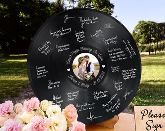 May include: A black vinyl record with a photo of a bride and groom in the center. The record is surrounded by white handwritten messages and hearts. The text "Can't Help Falling In Love" is written in cursive above the photo. The text "James & Emily - 09.15.2022" is written below the photo.
