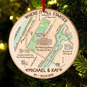 May include: A round wooden Christmas ornament with a map of New York City, including Central Park and the Metropolitan Museum of Art. The text "WHERE IT ALL STARTED" is at the top, with names and a date at the bottom.