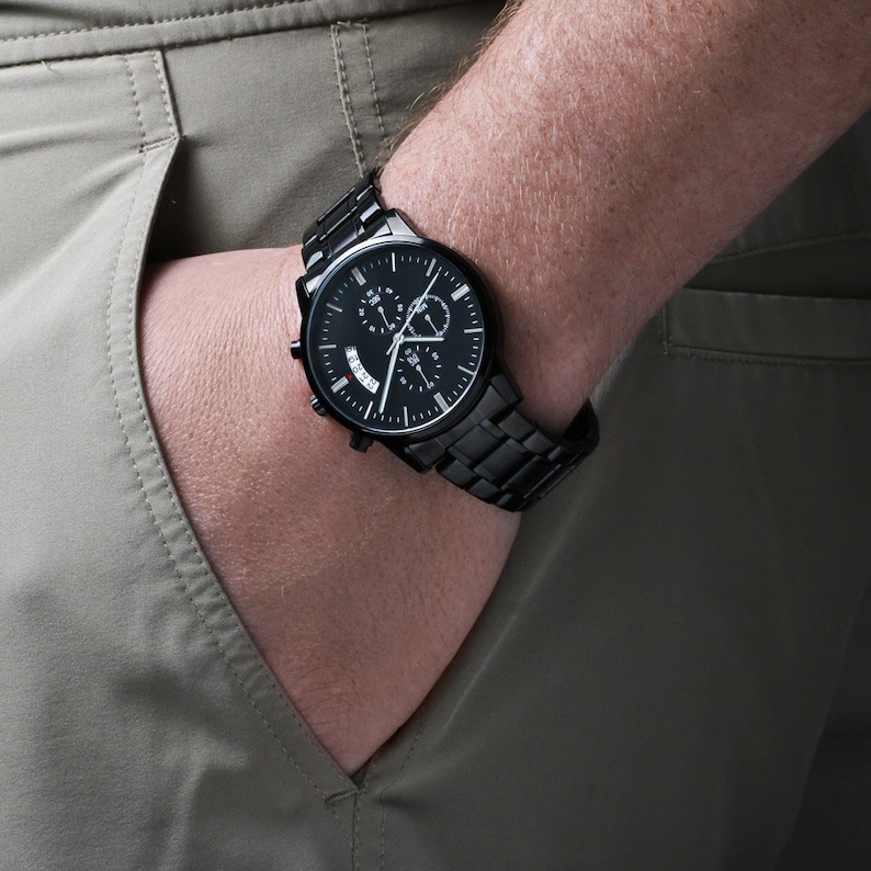 May include: A black chronograph wristwatch with a black metal band. The watch face has a black background with white markings and silver hands.