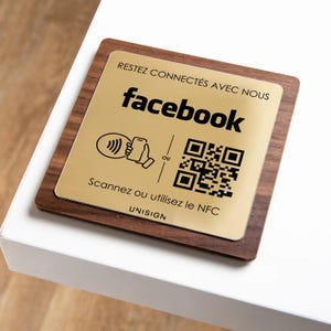 May include: A square wooden sign with a gold-colored metal plate. The plate has the Facebook logo and a QR code, along with the text "RESTEZ CONNECTÉS AVEC NOUS" and "Scannez ou utilisez le NFC".