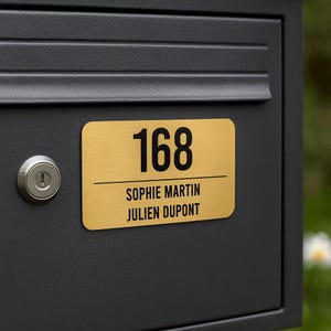 Könnte beinhalten: Ein schwarzer Briefkasten mit einer goldenen Adressplatte. Die Platte zeigt die Nummer "168" in fetter schwarzer Schrift sowie die Namen "SOPHIE MARTIN" und "JULIEN DUPONT". Auf der linken Seite ist ein silbernes Schloss zu sehen.