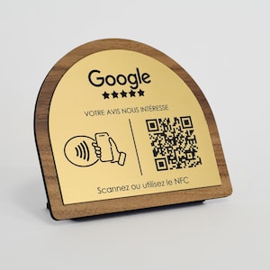 Op de afbeelding: Een houten bureau-bord met een goudkleurige metalen plaat. De plaat toont het Google-logo, vijf sterren en de tekst "VOTRE AVIS NOUS INTÉRESSE". Het bevat ook een QR-code en een afbeelding van een telefoon met een draadloos symbool.
