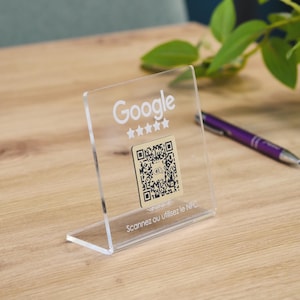 May include: A clear acrylic L-shaped sign stand featuring the white Google logo above five white stars and a central gold-colored square QR code. The base of the stand includes the white text Scannez ou utilisez le NFC printed on the front.