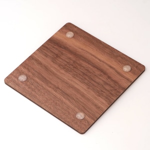May include: A square, wooden coaster with a rich brown color and visible wood grain. The coaster has four small, clear, rounded feet on the corners. The coaster is designed to protect surfaces from drink condensation.