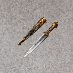 May include: A silver and gold dagger with a decorative handle and a sheath. The blade is engraved with the words "Half my soul".