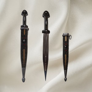 May include: Three decorative daggers with intricate designs and gold accents. The center dagger has the inscription "To Justice, My Beloved".