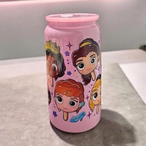 May include: Pink tumbler featuring cartoon images of Disney princesses as popsicles. The tumbler has a pink lid and a cylindrical shape. Decorative stars and a blue shoe accent the design. A fun and colorful drinkware item.