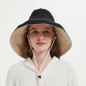 May include: A black and beige reversible sun hat with a wide brim. The hat has a drawstring chin strap and a black toggle. The hat is designed to provide sun protection.