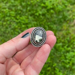 May include: A silver ring with an oval-shaped black and white stone set in a rope-like border.