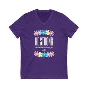 May include: A purple V-neck t-shirt featuring the text "BE STRONG and very courageous" in white, surrounded by a floral design in various colours. The shirt also includes the text "jaylane" and a Bible verse reference. The design is centered on the front.