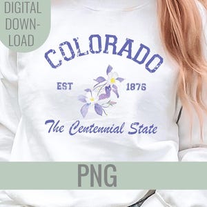 May include: White long-sleeved sweatshirt featuring the word "COLORADO" in distressed purple lettering. Below the word are the words "EST 1876" and a floral design. The phrase "The Centennial State" is printed below the floral design. The words "DIGITAL DOWNLOAD" and "PNG" are also visible.