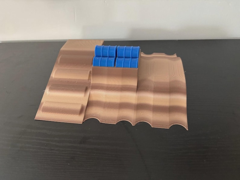 May include: A 3D-printed model of a desert landscape with a series of brown, layered terrain features. Four small blue barrels are positioned on the highest point of the landscape. The model is designed for tabletop gaming or display.
