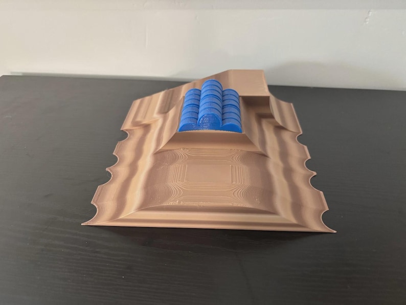 May include: A 3D-printed sculpture featuring a layered, light brown base with a textured surface and scalloped edges. Three blue cylindrical objects are stacked on top. The sculpture is displayed on a dark surface.