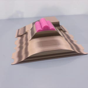 May include: A tan, layered, 3D-printed sculpture with a wavy edge. Three bright pink cylindrical objects are nestled in the center. The sculpture is on a light gray surface.