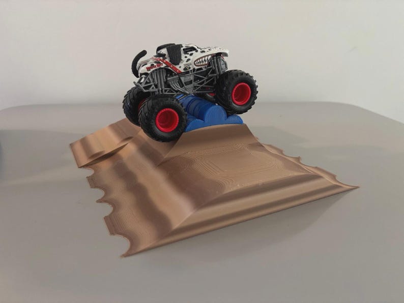 May include: A toy monster truck with a dalmatian-themed design, red accents, and large black tires with red rims, is positioned on a brown ramp with a blue barrel obstacle. The toy is designed for play and is suitable for children.
