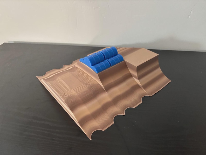 May include: A 3D-printed model featuring a brown, layered landscape with a series of blue cylindrical objects. The model has a textured surface and a scalloped edge. The design is geometric and modern.