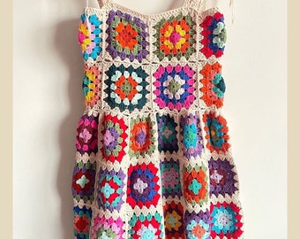 Puede incluir: Un vestido de crochet colorido con un patrón de cuadrados de la abuela. El vestido tiene un corpiño ajustado y una falda acampanada. Las tiras son finas y se atan en los hombros. El vestido está hecho en una variedad de colores, incluyendo rojo, naranja, amarillo, verde, azul, morado y rosa.