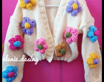 Puede incluir: Un cárdigan blanco de punto con cuello en V y mangas largas. El cárdigan está decorado con flores de ganchillo de colores en tonos rosa, azul, amarillo y morado.