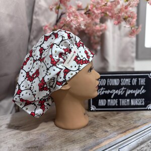 May include: White scrub cap with a Hello Kitty print. The cap has a red and white label that says "Vnsh Scrubs".