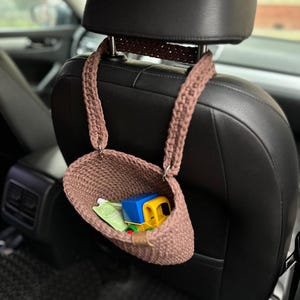 Pu&ograve; includere: Un cestino appeso in crochet marrone con un camion giocattolo all'interno. Il cestino &egrave; appeso allo schienale di un sedile auto.