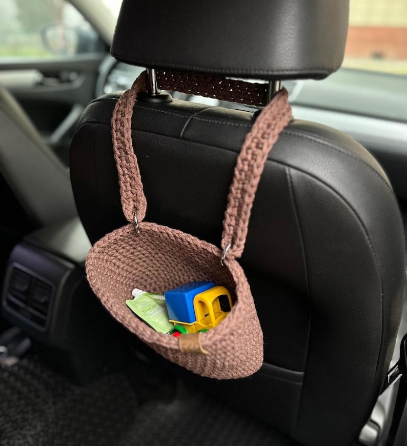 Pu&ograve; includere: Un cestino appeso in crochet marrone con un camion giocattolo all'interno. Il cestino &egrave; appeso allo schienale di un sedile auto.