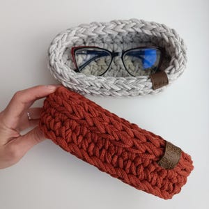 May include: Two crocheted baskets, one gray and one rust colored. The gray basket has a pair of glasses inside. Both baskets have a leather tag with the word "EKO" on them.