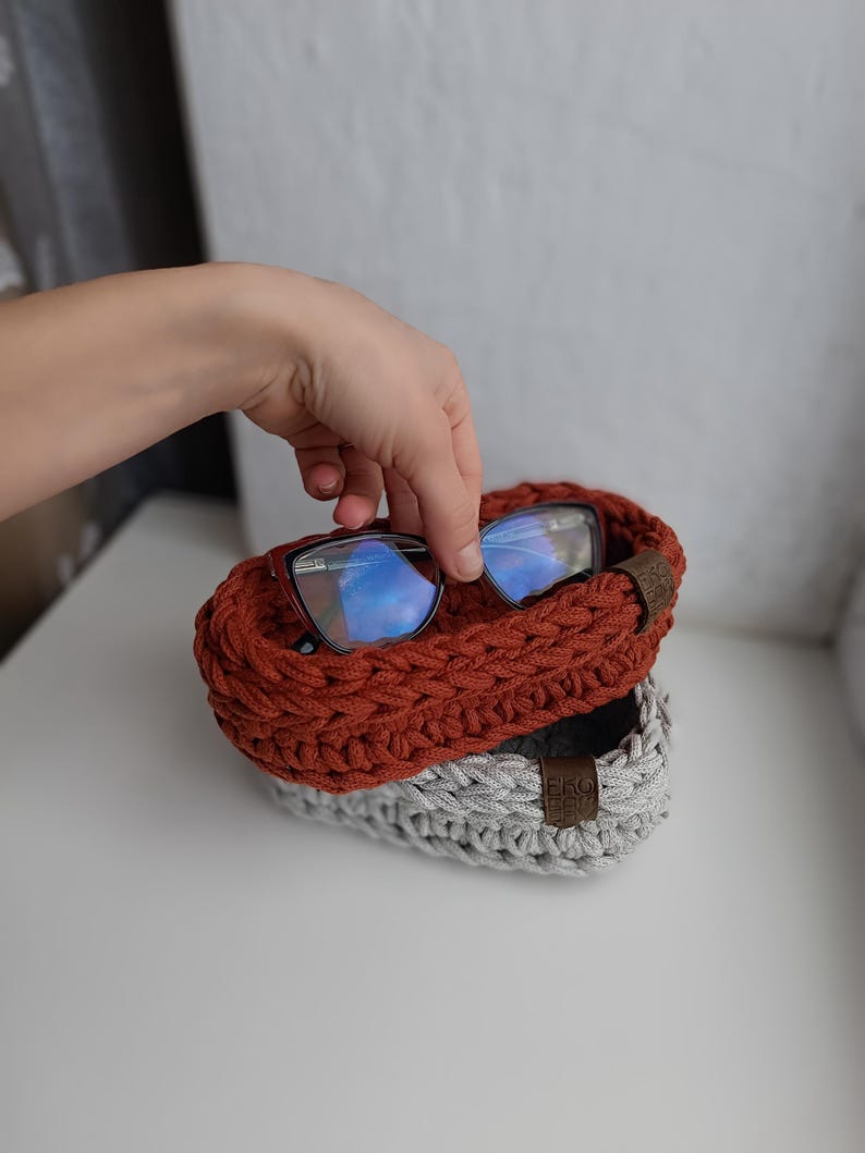 May include: Two crocheted baskets, one red and one gray, with a pair of blue-tinted glasses resting on top of the red basket.